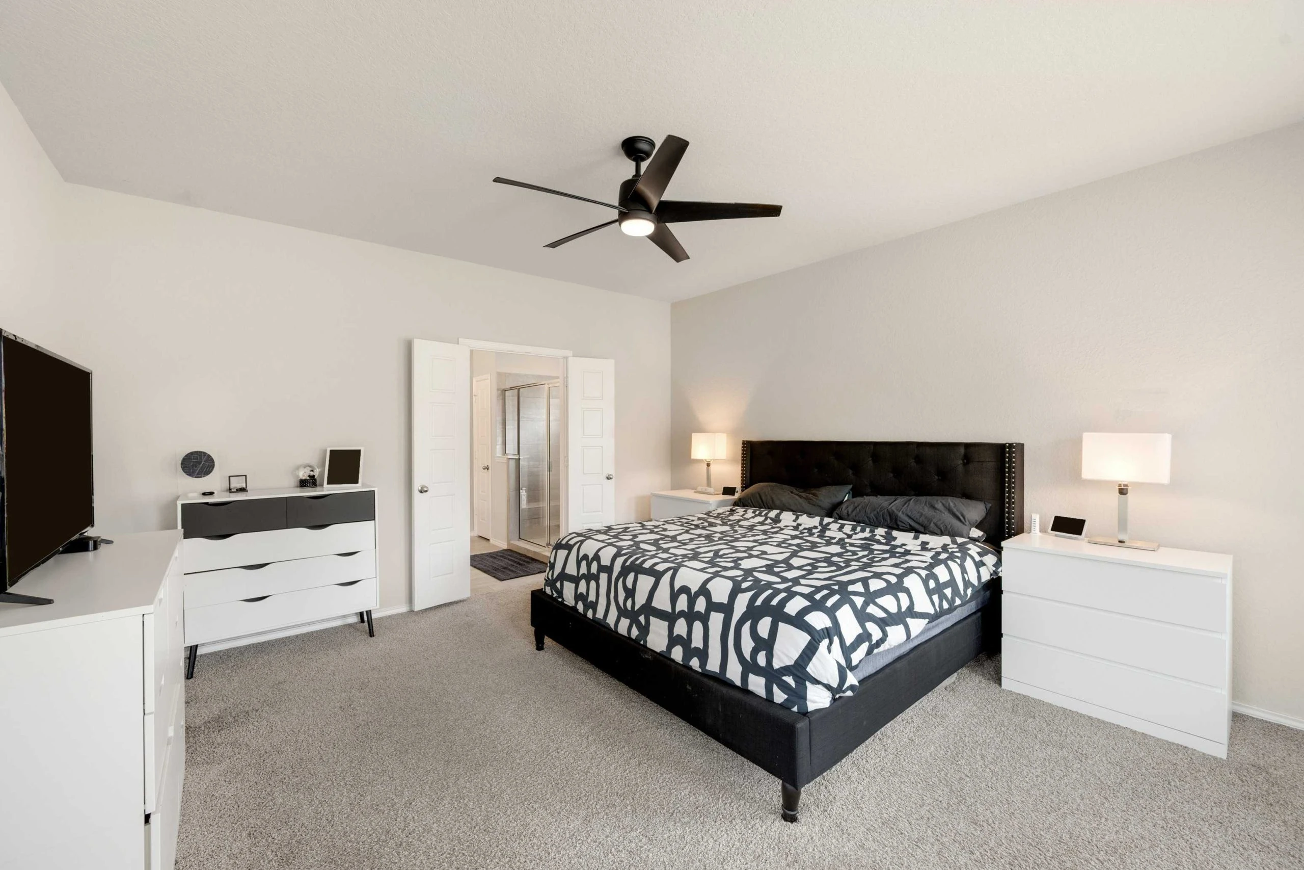 A bedroom with a bed, dresser and ceiling fan.