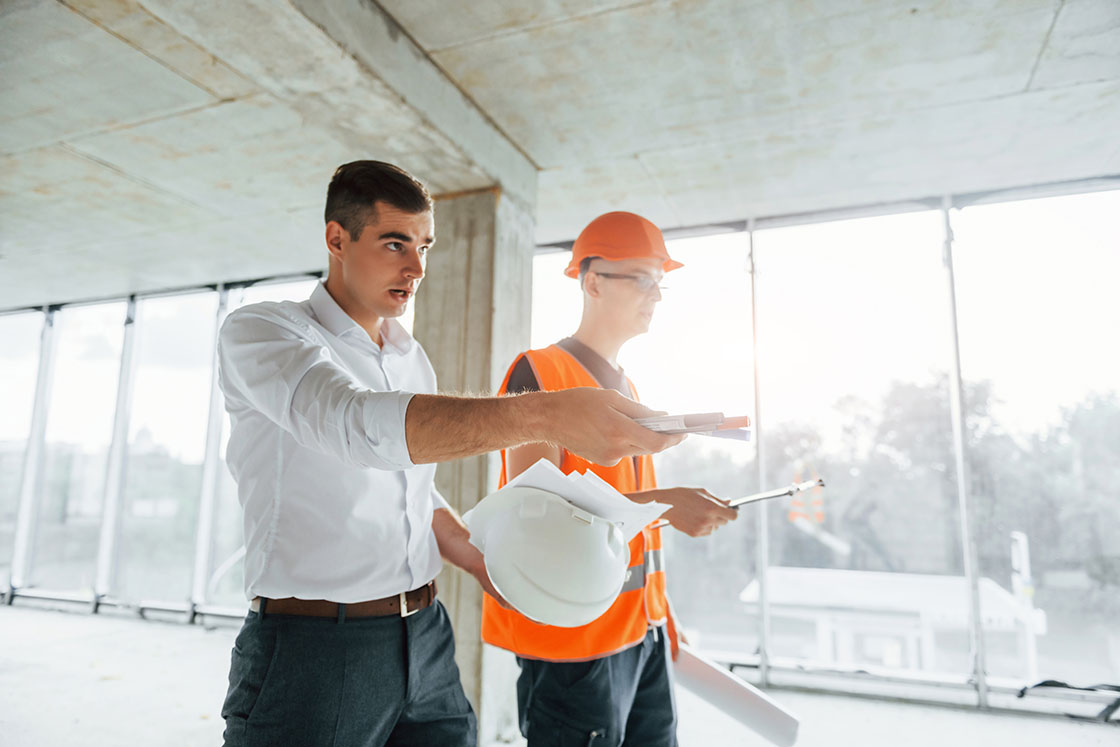 Two men in hard hats standing in front of a building.